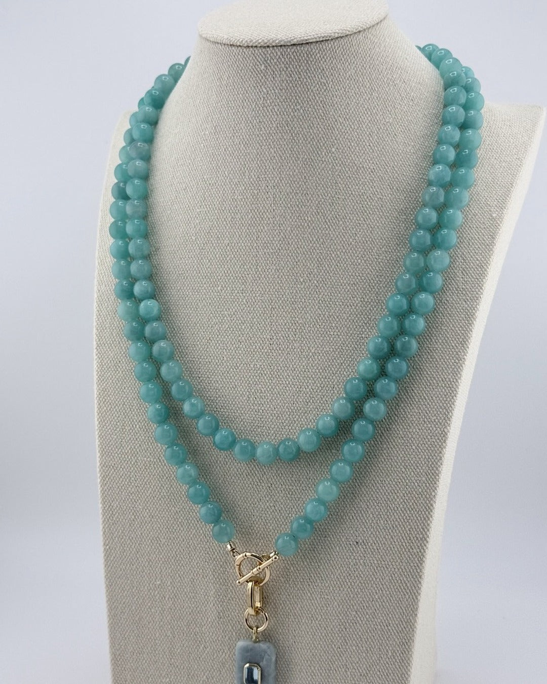 Long amazonite bead necklace worn doubled on a linen bust with a carved aquamarine pendant set with blue topaz