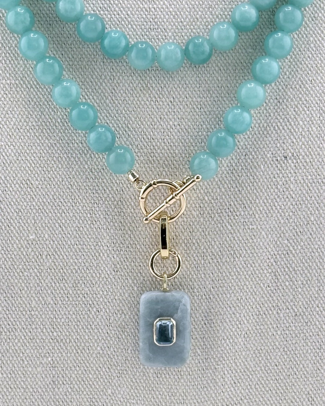 Close view of the carved aquamarine pendant with a bezel-set emerald-cut blue topaz and gold toggle clasp