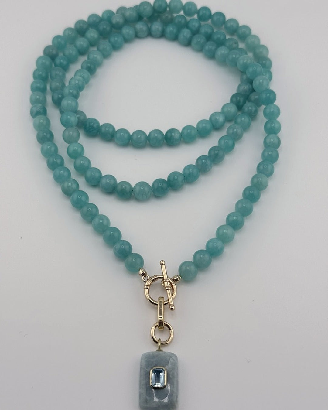Flatlay of the full-length amazonite strand coiled with the aquamarine blue topaz pendant