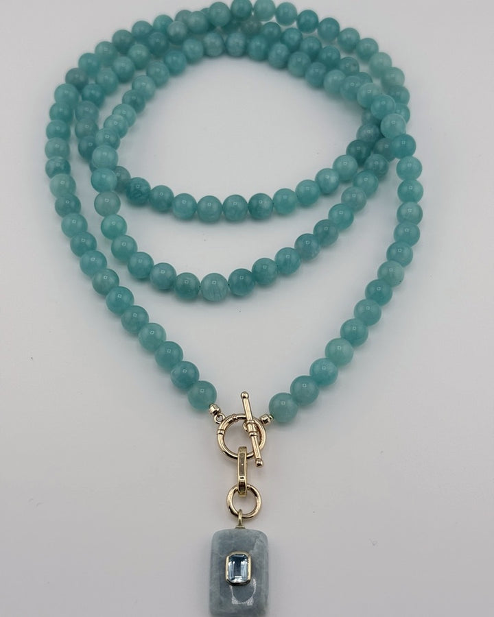 Flatlay of the full-length amazonite strand coiled with the aquamarine blue topaz pendant