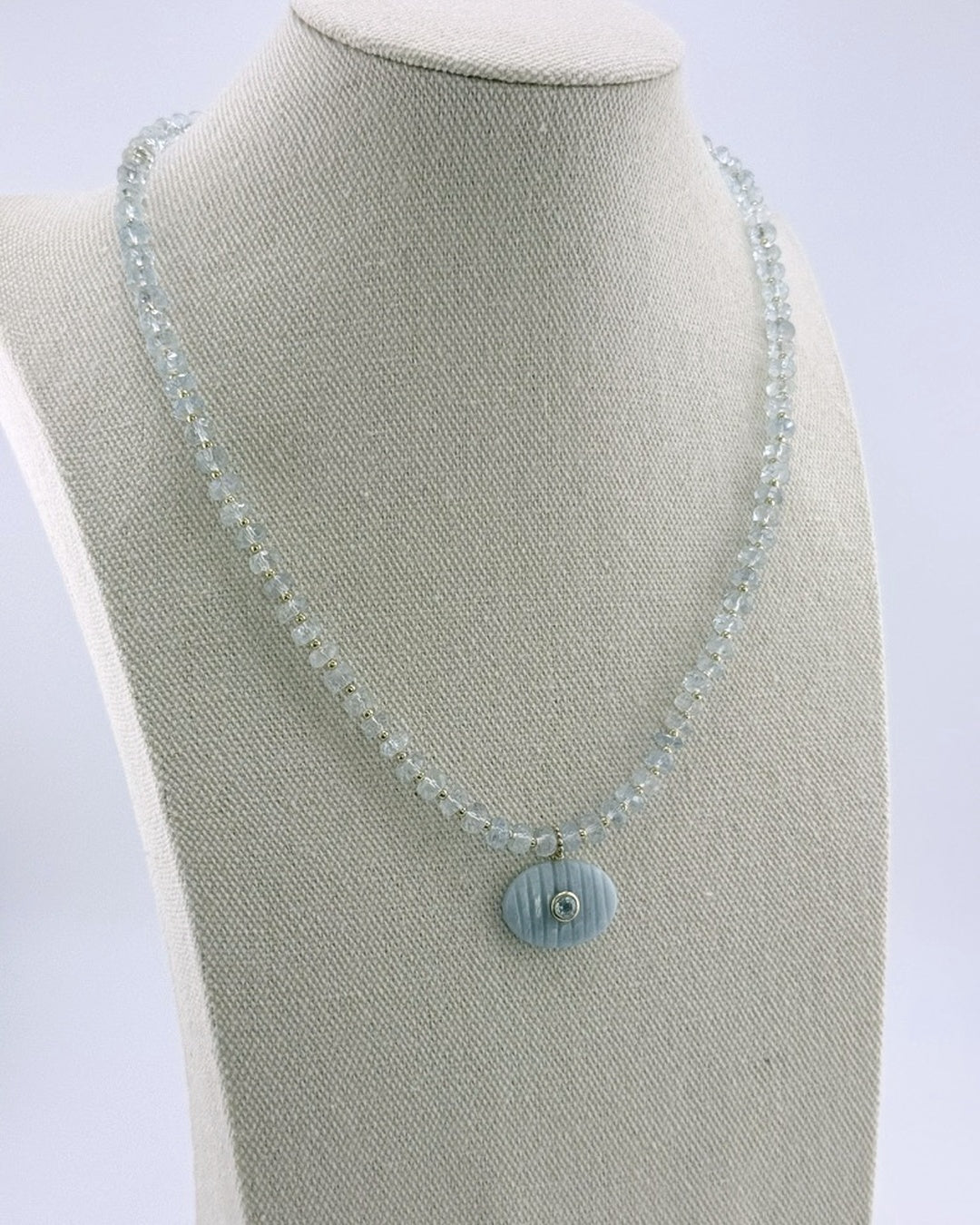 Pale aquamarine necklace with a carved aquamarine oval pendant, full view on a display bust