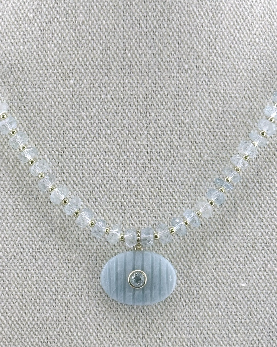 Detail of the carved aquamarine oval pendant with a faceted aquamarine center on the faceted aquamarine strand