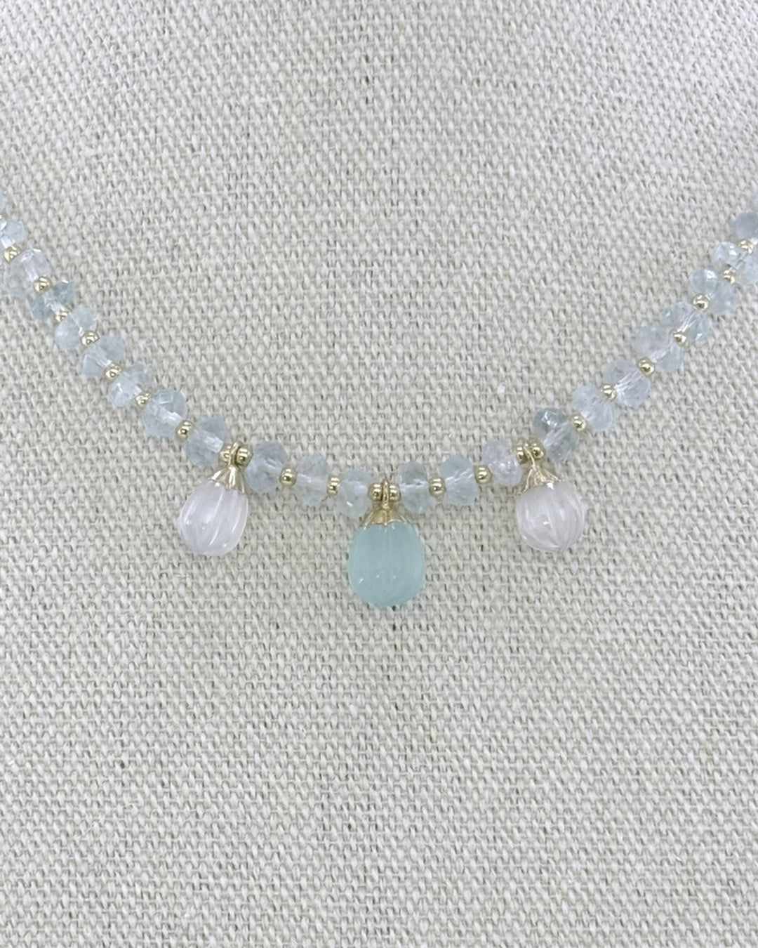 Detail of the three carved drops — a blue chalcedony center flanked by two moonstones — capped in gold on the faceted aquamarine strand