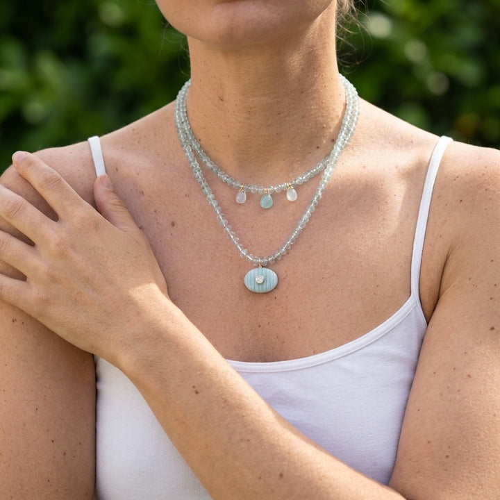 woman wearing the aquamarine drops necklace layered with a longer aquamarine pendant necklace, poolside in natural light