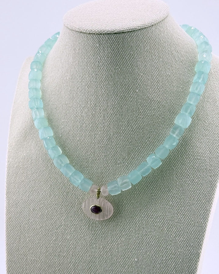 Close view of the carved rose quartz oval pendant with a bezel-set faceted ruby at its center