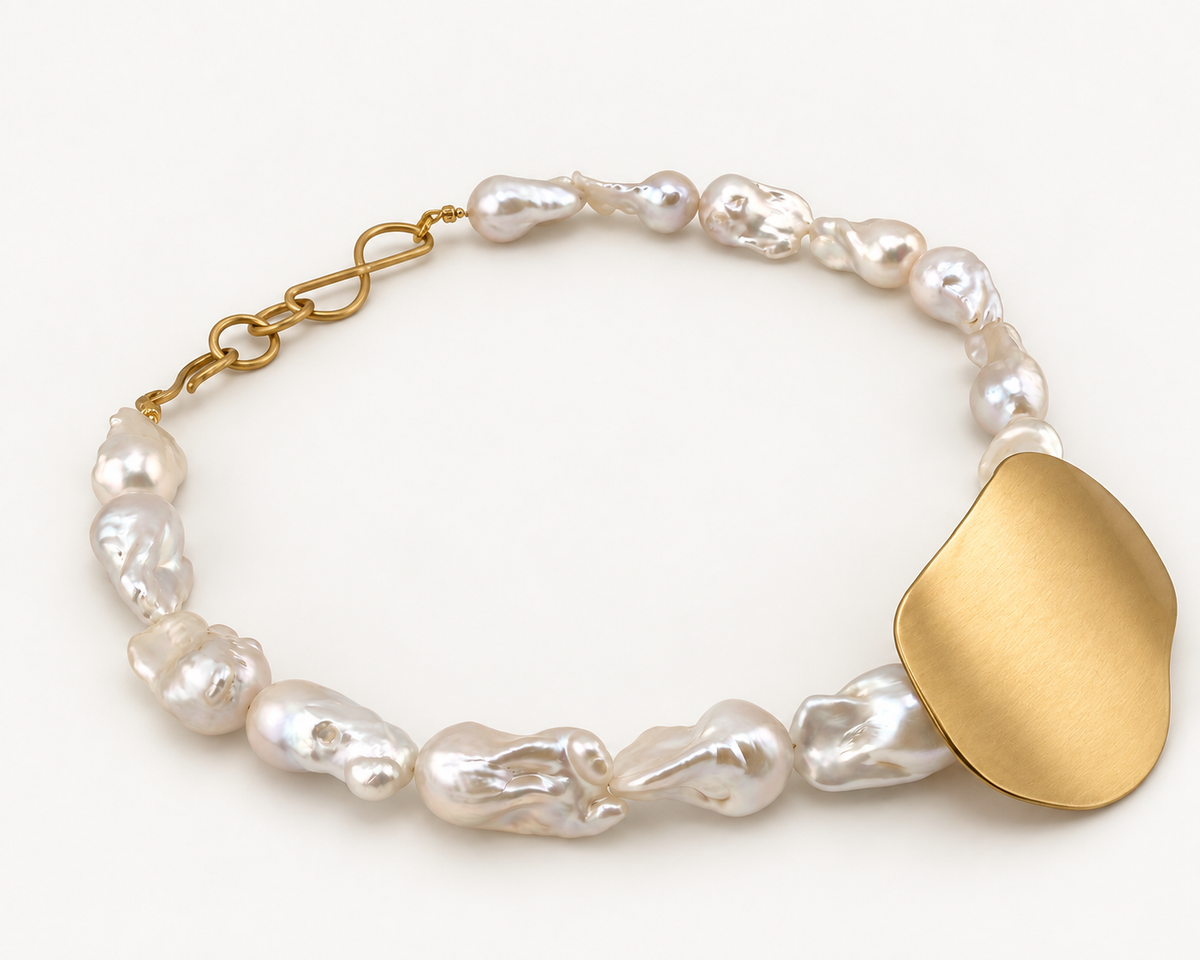 Side view of the Bibi necklace showing the curve of the brushed brass pendant and the brass hook clasp