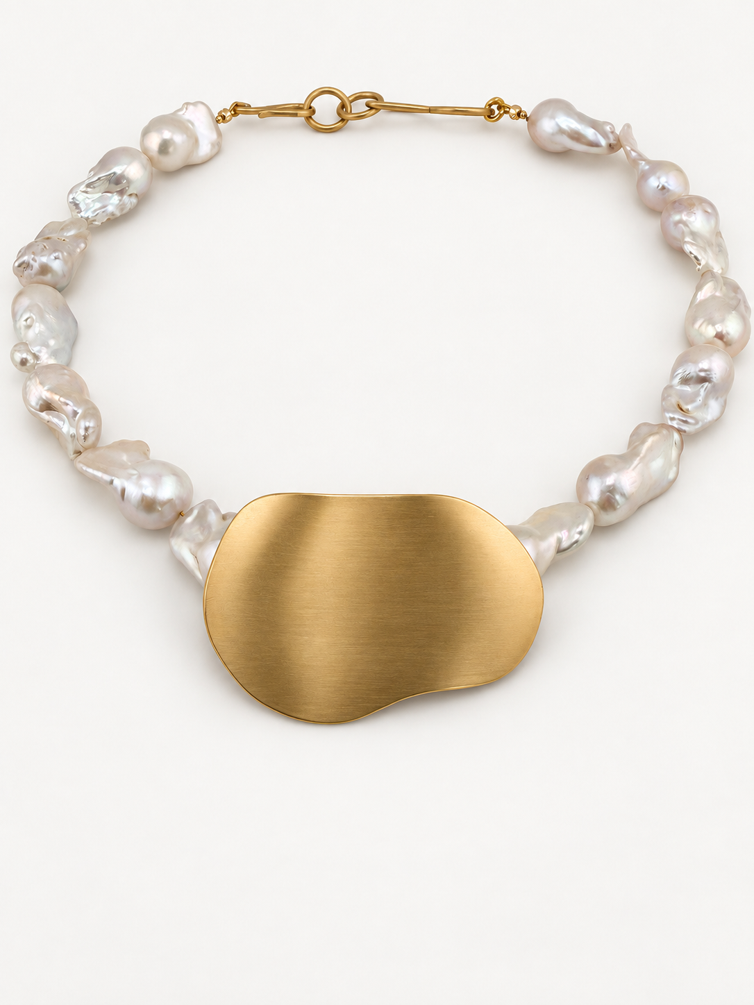 Bibi necklace: large white baroque cultured pearls around a freeform brushed brass pendant, laid flat on a white background