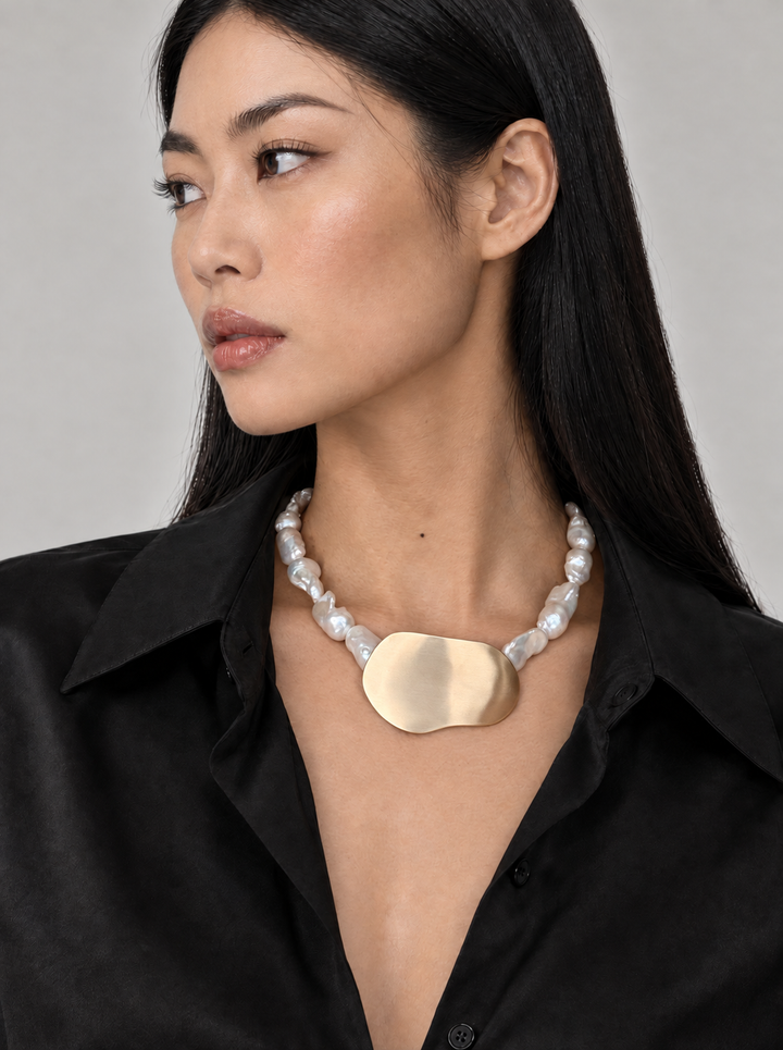 Bibi baroque cultured pearl and brass necklace worn at the collarbone with an open-collar black shirt