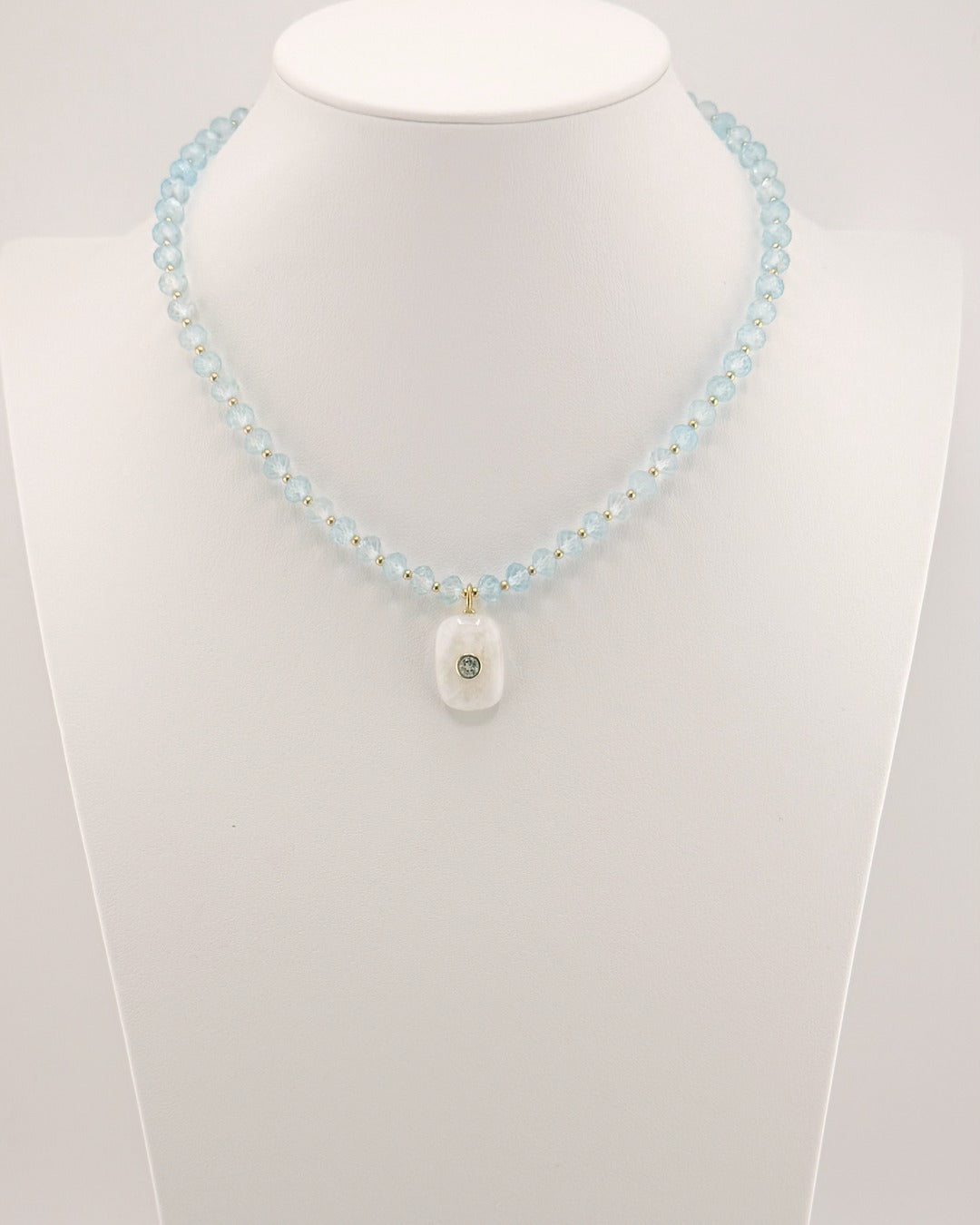 Blue topaz bead necklace with a carved moonstone pendant set with a blue topaz, on a bust