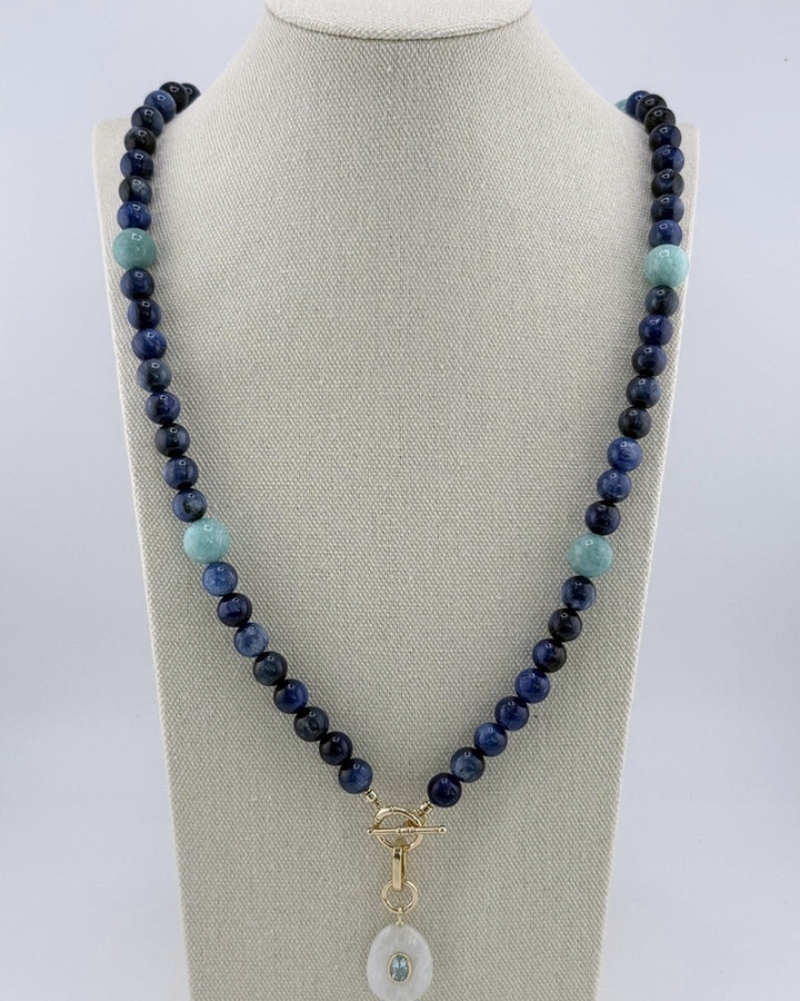 Deep-blue kyanite bead necklace with aqua amazonite accents and a carved moonstone pendant set with blue topaz, on a linen bust