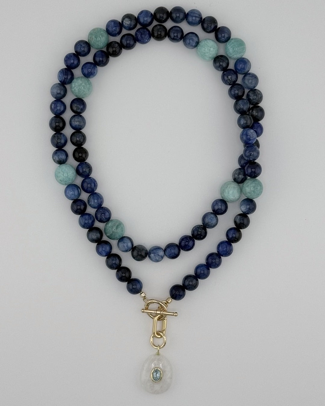 Flatlay of the kyanite and amazonite strand coiled with the moonstone and blue topaz pendant