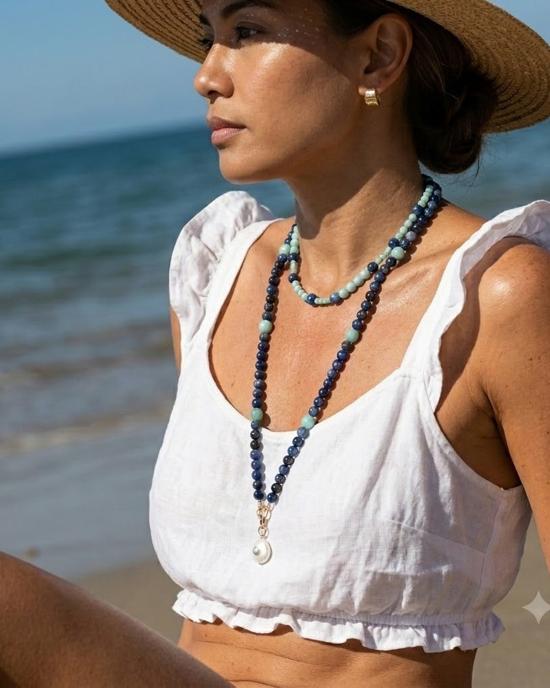 Model in a white linen top and straw hat on the beach wearing the kyanite and amazonite necklace stacked and doubled with the moonstone pendant