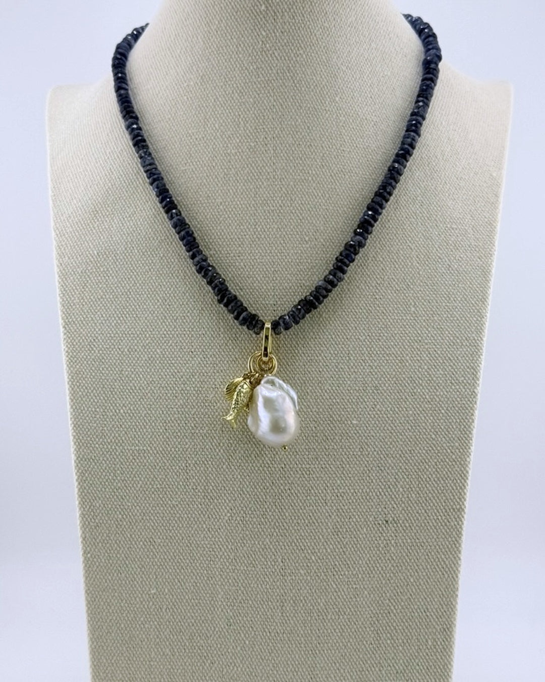 Navy kyanite necklace with a baroque pearl and gold charm drop, front view on a display bust
