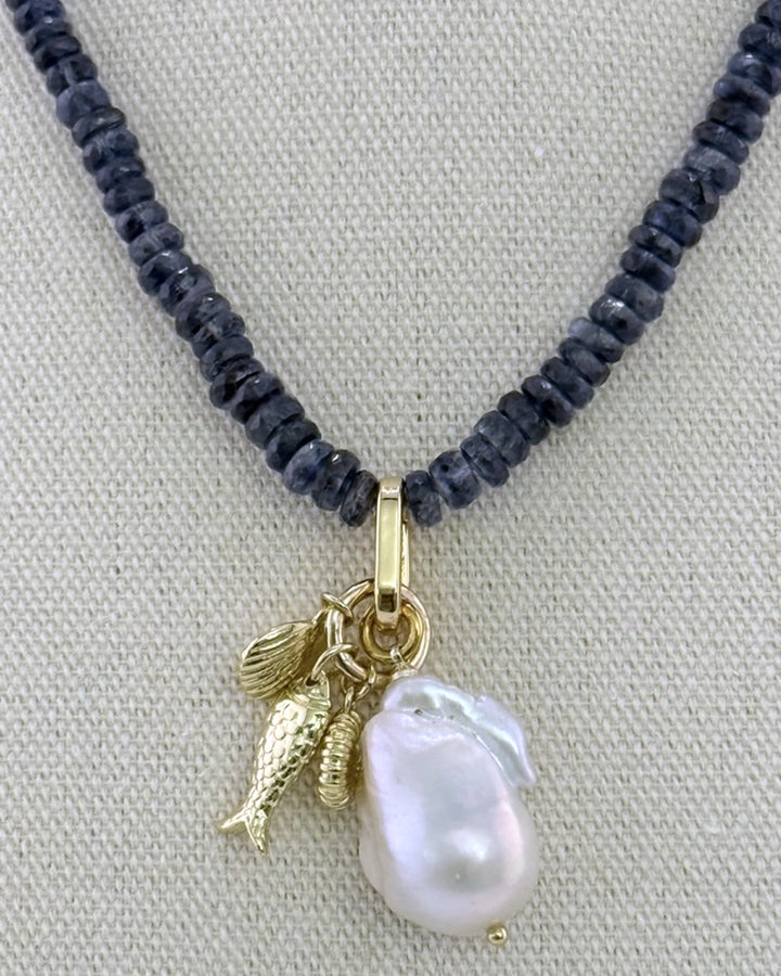 Detail of the baroque pearl drop with 18k gold-plated fish, shell, and spiral charms on the faceted kyanite strand