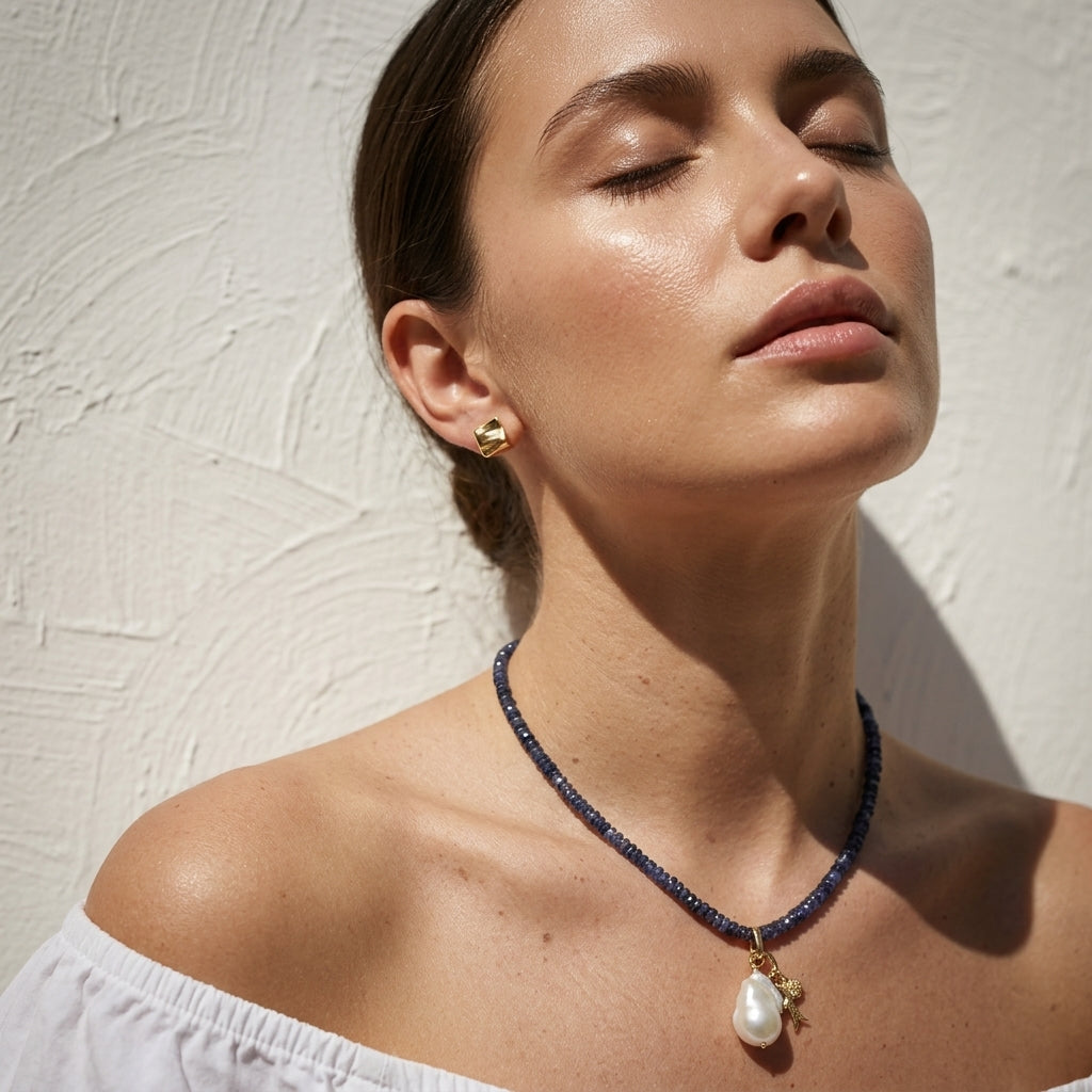woman in a white off-shoulder top wearing the kyanite and pearl drop necklace in golden sunlight