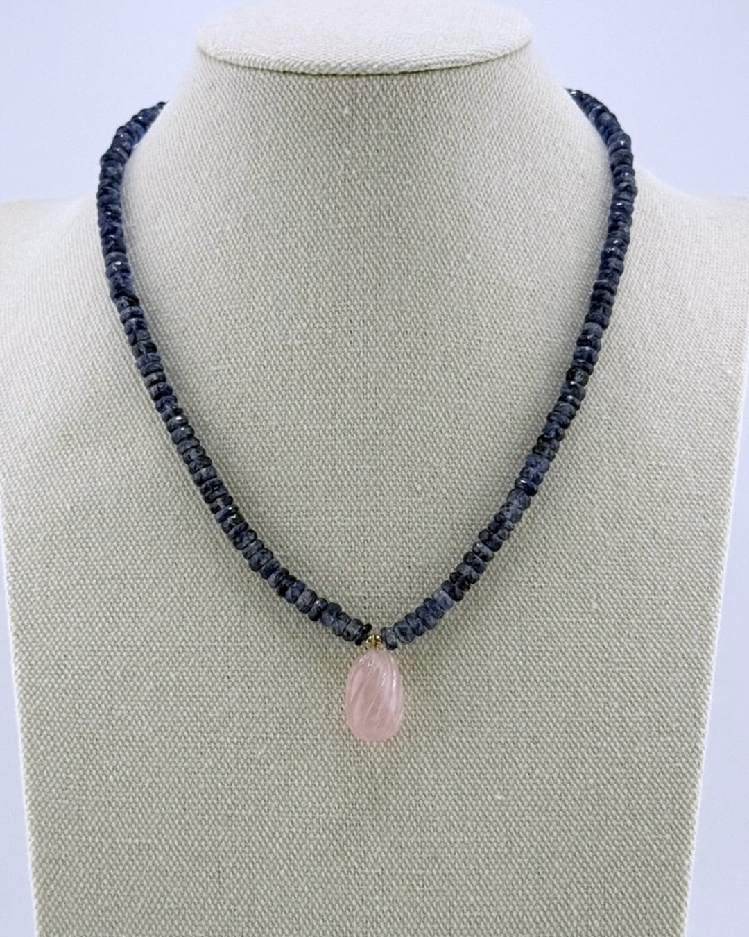 Navy kyanite necklace with a carved rose quartz teardrop drop, front view on a display bust