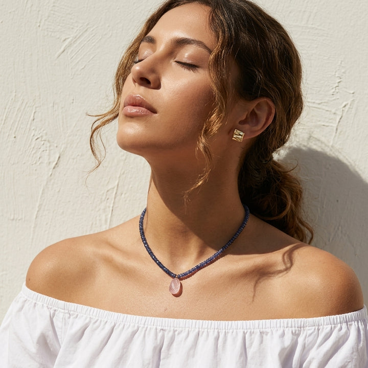 woman in a white off-shoulder top wearing the kyanite and rose quartz necklace in golden sunlight