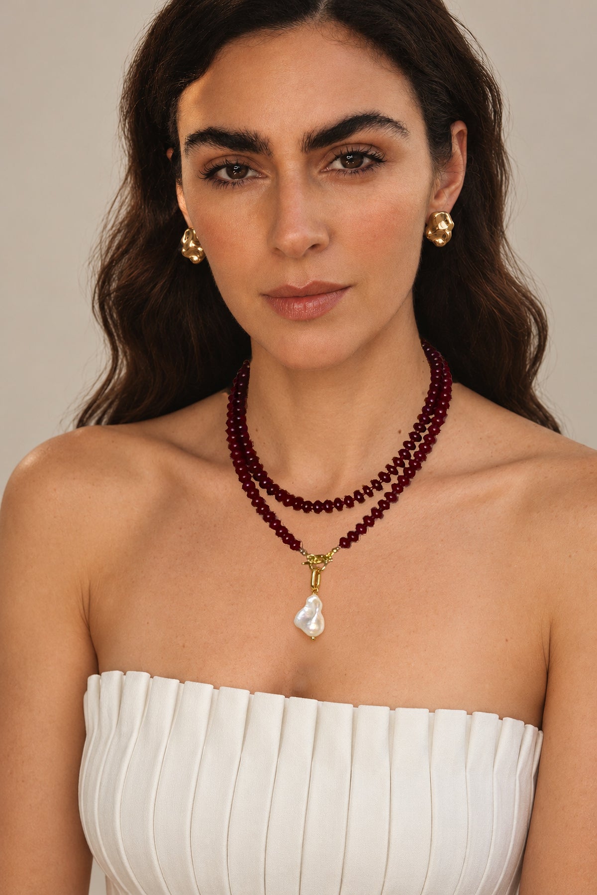 Lulu Necklace in Burgundy worn doubled with a cultured baroque pearl charm, on a model in a white strapless top