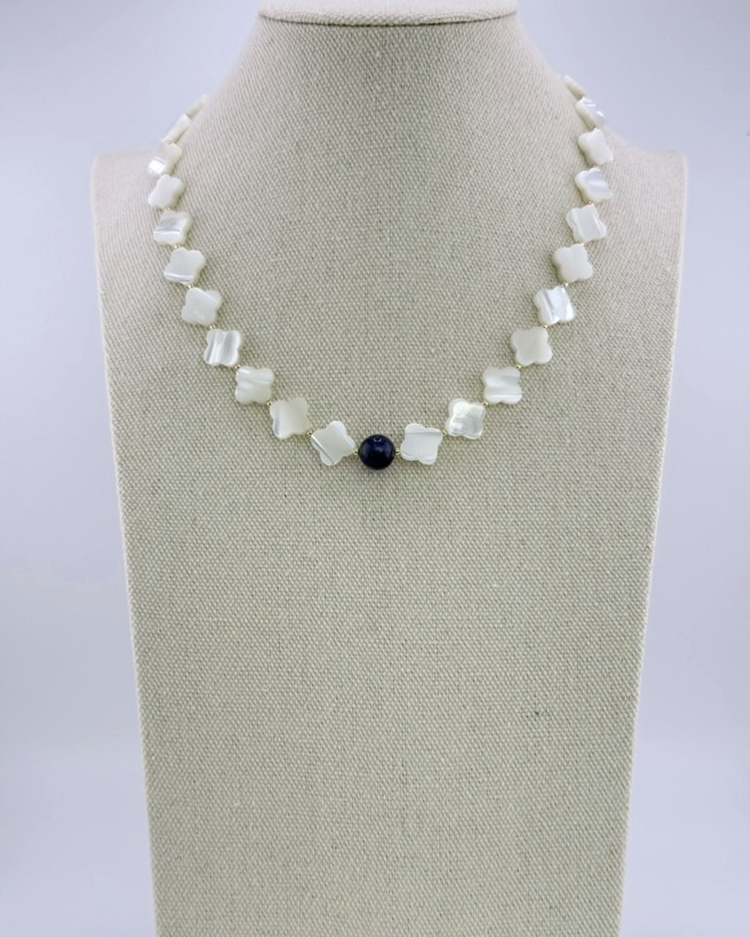 Mother of pearl quatrefoil necklace with a single navy kyanite bead at the center, front view on a display bust