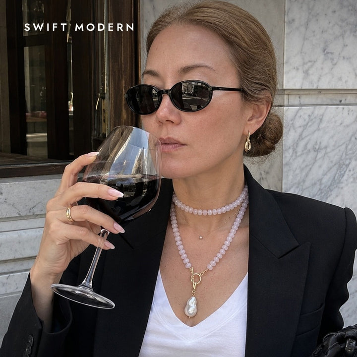 Close-up of the rose quartz and peridot necklace worn doubled at the collarbone with its baroque pearl pendant, styled with a white tee and black blazer