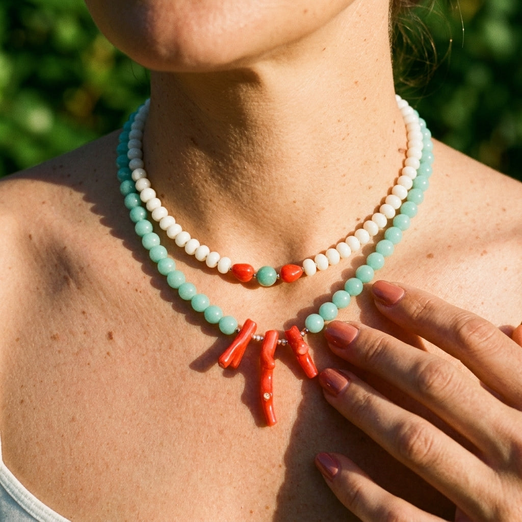 the white jade and coral necklace layered with an amazonite and coral necklace against green foliage