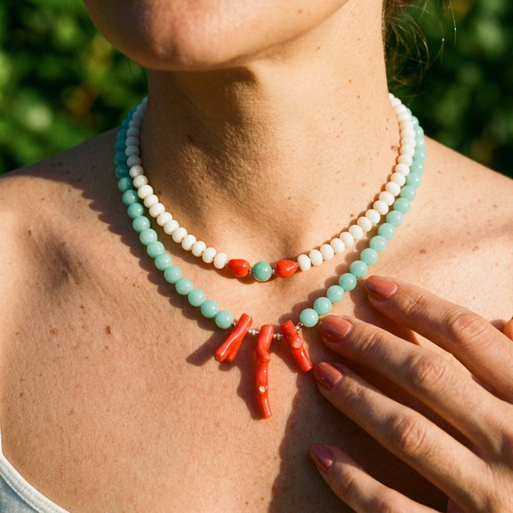 the white jade and coral necklace layered with an amazonite and coral necklace against green foliage