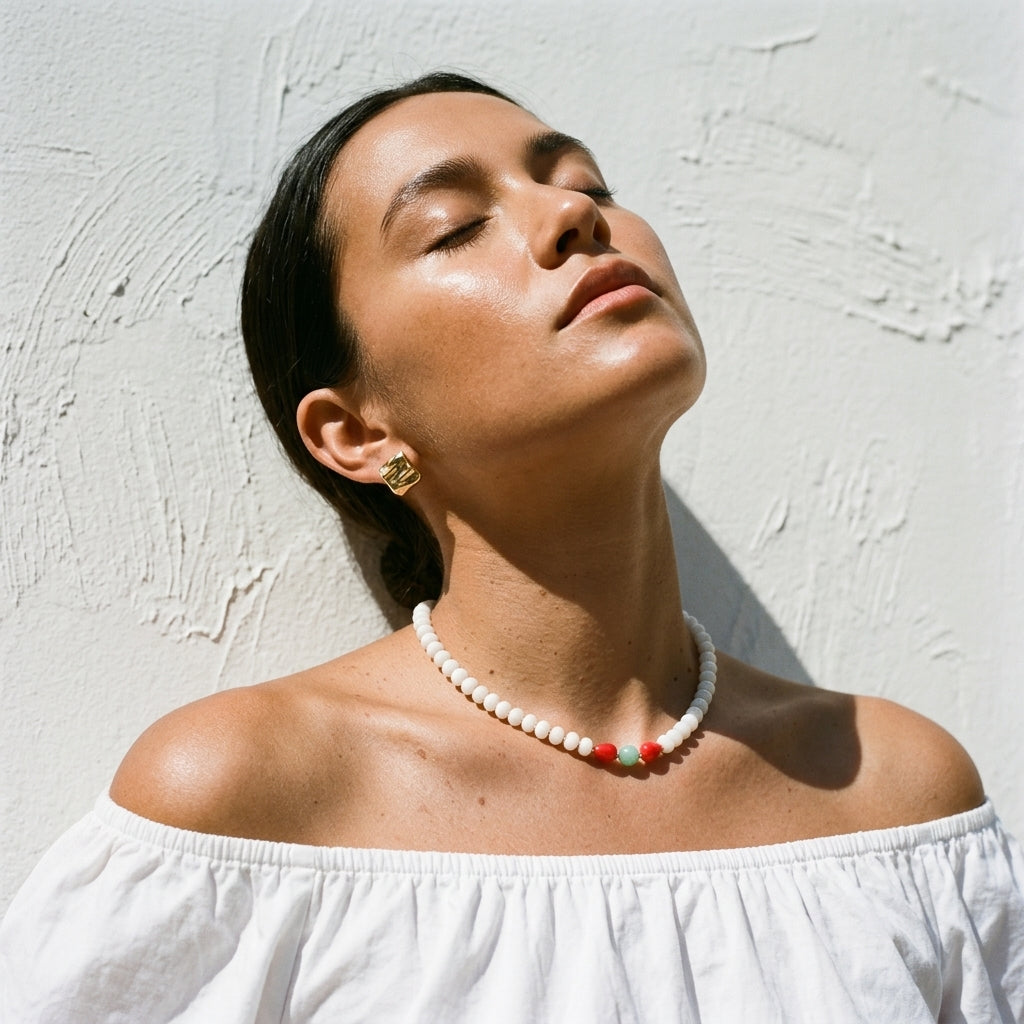 woman in sunlight against a stucco wall wearing the white jade and coral necklace with an off-shoulder white top